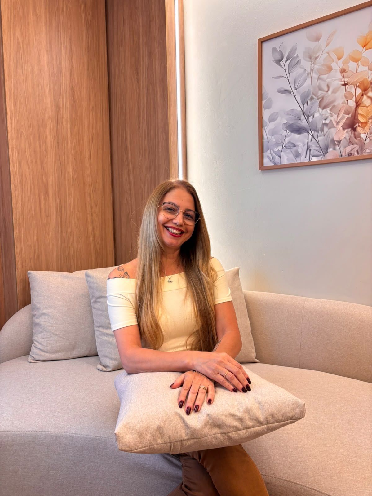 Viviane Gatis sentada no sofá do consultório, sorrindo, com uma almofada no colo.